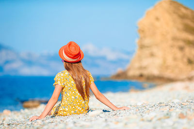 Woman sitting on rock at beach against sky