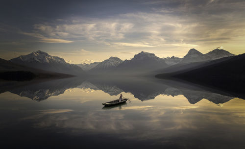 People sailing in boat at lake against sky during sunset