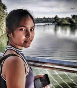 Portrait of young woman standing by lake against sky