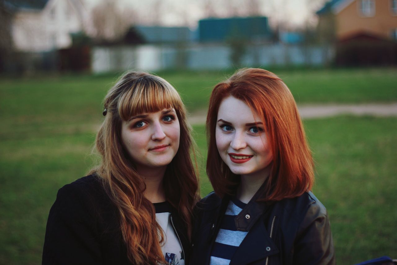 two people, real people, focus on foreground, young women, young adult, looking at camera, portrait, togetherness, day, front view, grass, redhead, leisure activity, outdoors, lifestyles, smiling, friendship