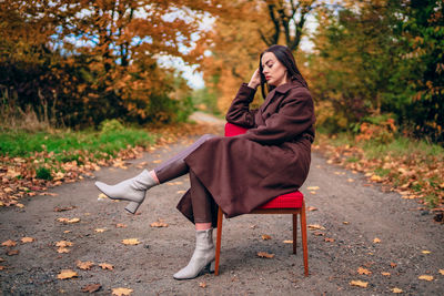 Young beautiful woman with old armchair on the country lane in autumn