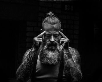 Portrait of man swith a beard and tattoos tanding against black background
