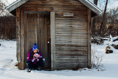 Girl eating snow against wooden cabin