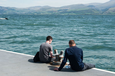 Rear view of friends sitting on pier over sea