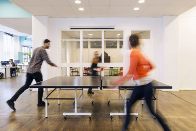 Blurred motion of business people playing table tennis in creative office