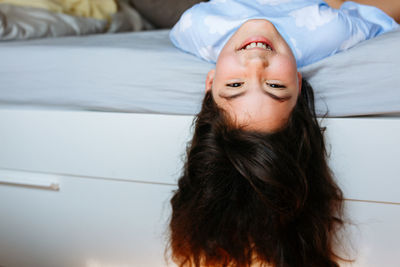 Smiling girl with long hair lying on the bed with head down