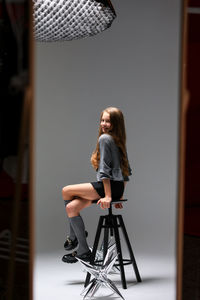 A trendy studio portrait capturing the essence of a young woman sitting gracefully on a stool