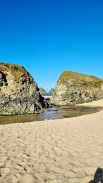 Scenic view of rocky beach against clear blue sky