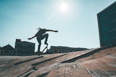 Low angle view of man jumping on built structure against sky