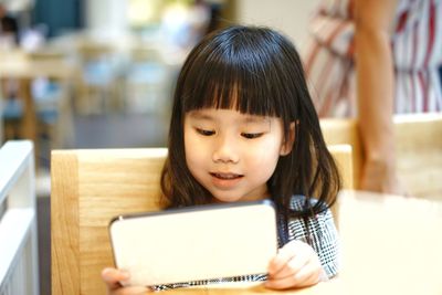 Close-up of girl using digital tablet while sitting on chair