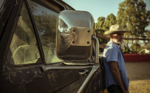 Closeup of side mirror of an old, dirty truck with adult man in background