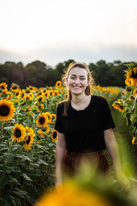 Portrait of smiling young woman standing by sunflowers