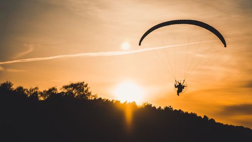 Silhouette person paragliding against sky during sunset