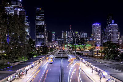 High angle view of light trails on road amidst buildings in city at night