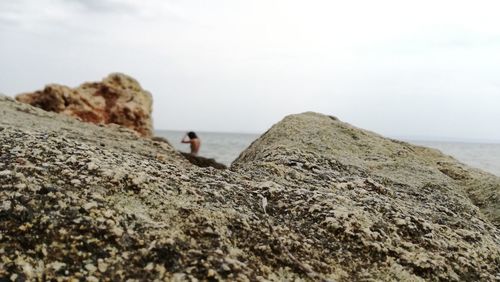 Rear view of man standing on rock by sea against sky