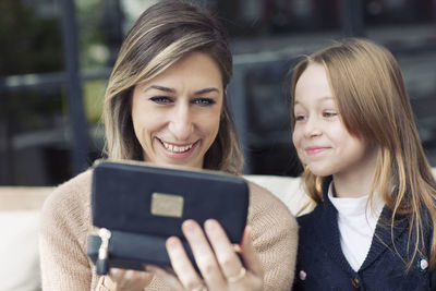 Close-up of mother and daughter using phone while sitting on sofa