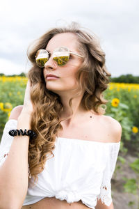 Portrait of young woman wearing sunglasses while standing on field