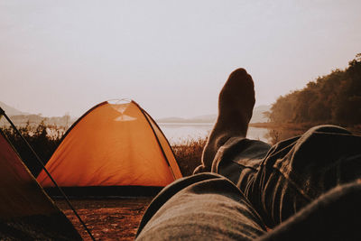 Low section of person relaxing at tent against sky