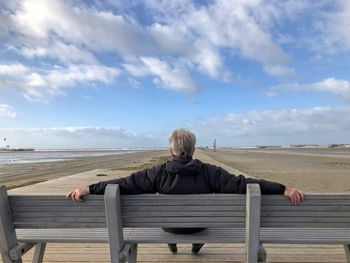 Rear view of man sitting on bench against sky