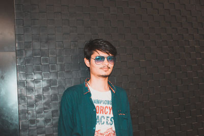 Portrait of young man standing against brick wall