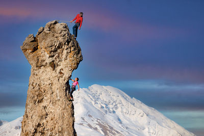 Man climbing rock on mountain against sky