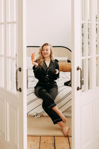 A happy pretty young woman in pajamas is resting and having breakfast in bed in a cozy apartment