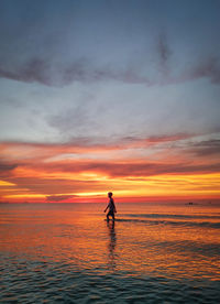 Silhouette man standing in sea against sky during sunset