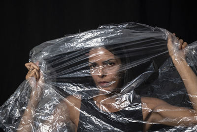 Model portrait with clear plastic in front of her face against black background. 