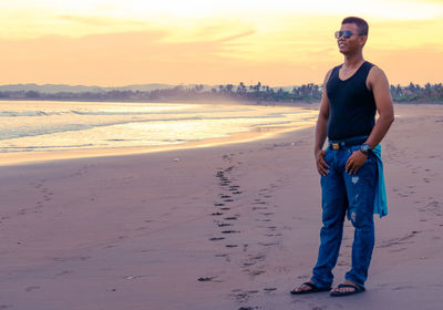 Full length of young man standing on beach during sunset