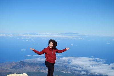 Happy woman with arms outstretched standing against clouds covered mountain