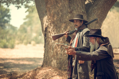 Men aiming guns while standing in forest