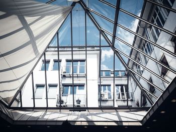 Low angle view of cloudy sky through transparent glass ceiling