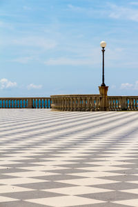 Street lights on footpath by sea against sky