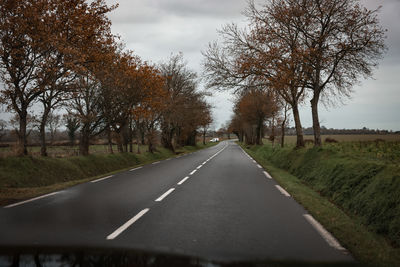 Empty road amidst bare trees against sky