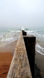 Wooden posts on beach against cloudy sky