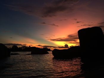 Silhouette rocks at sea against sky during sunset