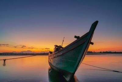 Sailboats moored in sea against sky during sunset