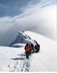 Rear view of hikers walking in row on snowcapped mountain during winter