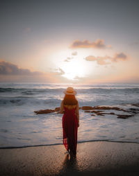 Rear view of woman standing on beach during sunset