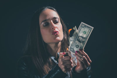 Close-up of woman puckering lips while burning dollar note against black background