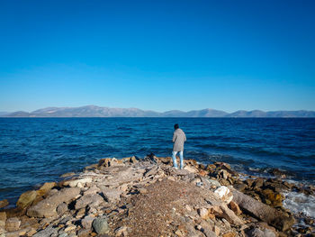 Young man standing on rocks while looking at sea