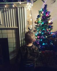 Boy standing at illuminated christmas tree at home