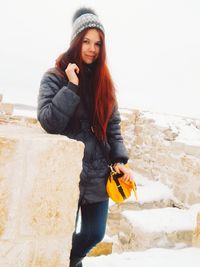 Portrait of young woman standing on snow against clear sky