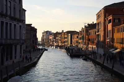 Canal amidst buildings in city against sky during sunset