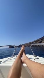 Low section of woman in boat on sea against clear blue sky