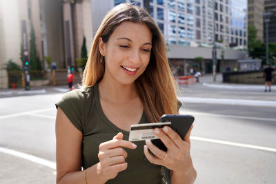 Fashion girl using credit card and smartphone for shopping online outdoors