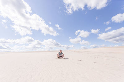 Man sitting on sand dune in desert against sky