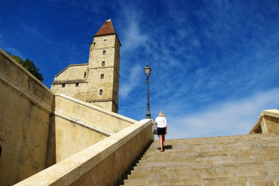 Low angle view of woman moving up on steps against blue sky