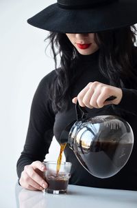 Midsection of woman pouring tea in cup at table against white background