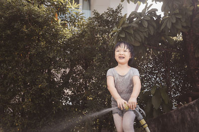 Funny moment of 3 year old asian kid playing water with garden hose in backyard. 